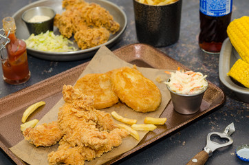 Dinner table with fried chicken wings and strips, roasted potatoes, french fries, coleslaw and sauces. Homemade southern fried chicken. Fried chicken meal