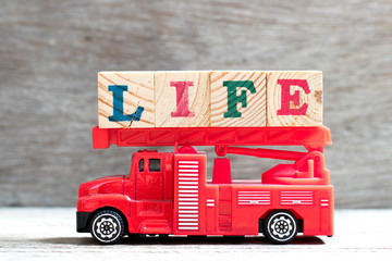 Toy fire ladder truck hold letter block in word life on wood background