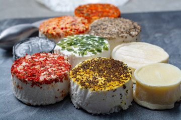 Assortment of French fresh white soft goat cheeses with different tastes topping made with herbs, paprika, indian curry, bruscetta, chives and dried tomatoes