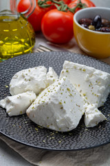 Fresh young soft white Feta cheese on black plate seasoned with dried oregano herb