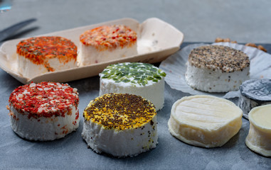 Assortment of French fresh white soft goat cheeses with different tastes topping made with herbs, paprika, indian curry, bruscetta, chives and dried tomatoes