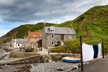 Single row of houses of Crovie coastal fishing village on Gamrie Bay North Sea Aberdeenshire Scotland UK with red telephone box and wash on line