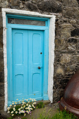 Blue door with daisies of stone house and upside down cauldron in coastal fishing village of Crovie Banff Aberdeenshire Scotland UK