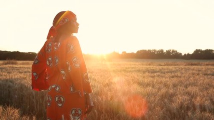 HD Video clip of African woman in traditional clothes standing in a field of crops looking to the sun at sunset or sunrise