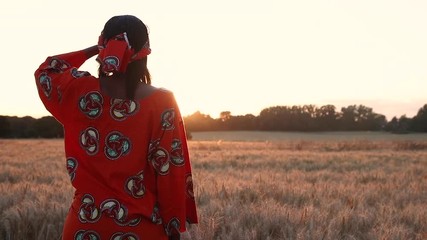 HD Video clip of African woman in traditional clothes standing in a field of crops looking to the sun at sunset or sunrise