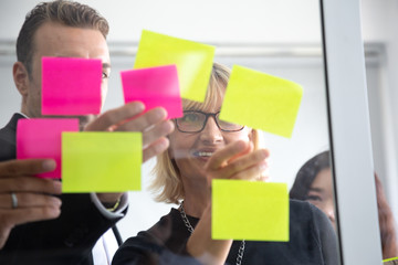 IT worker tracking his tasks on kanban board. Using task control of agile development methodology. Team members attaching sticky note to scrum task board in the office