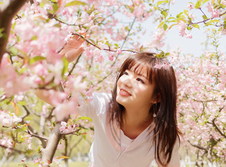 Outdoor portrait of beautiful young Chinese girl smiling among blossom cherry tree brunch in spring garden, beauty, summer, emotion, expression and people lifestyle concept.
