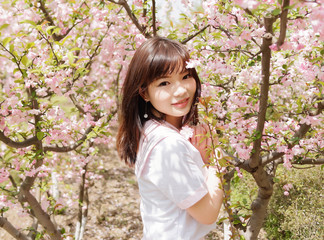 Outdoor portrait of beautiful young Chinese girl smiling among blossom cherry tree brunch in spring garden, beauty, summer, emotion, expression and people lifestyle concept.