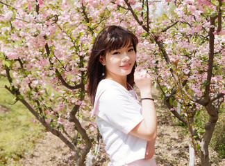 Outdoor portrait of beautiful young Chinese girl smiling among blossom cherry tree brunch in spring garden, beauty, summer, emotion, expression and people lifestyle concept.