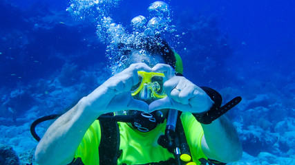 Scuba diving husband telling his wife that he loves her with heart shaped fingers.  Proposal, love,...