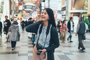 beautiful young girl holding camera standing on street in famous shopping area in osaka japan....