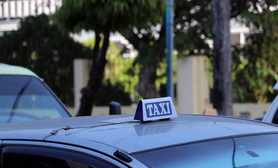 Taxi light sign or cab sign in white and blue color with white text on the car roof at the street.