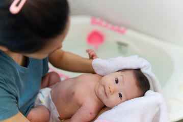Asian mother dry her newborn baby hair with towel after rinsing shampoo from the hair in bathroom....