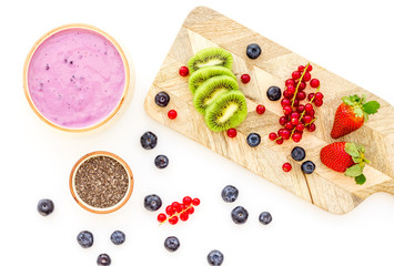 Naklejka na ściany i meble Preparing healthy fruit smoothie. Acai smoothie bowl near cutting board with fresh fruits, berries, chia seeds on white background top view