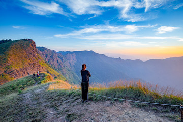 Fototapeta premium Woman waiting for sunrise at Sanknokwua (San Knok Wua) hill at Khao Laem National Park, Kanchanaburi, Thailand. Abstract of freedom and Peaceful with natural clear sky background
