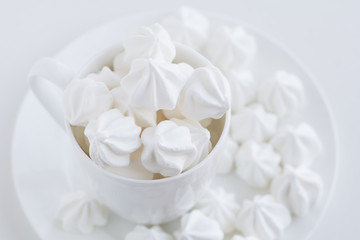 Fototapeta na wymiar The white merengue in the white tea cup on white background, on white plate, top view