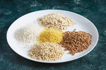 Scattered grains in a pile on a white plate. Buckwheat, rice, peas, oatmeal.