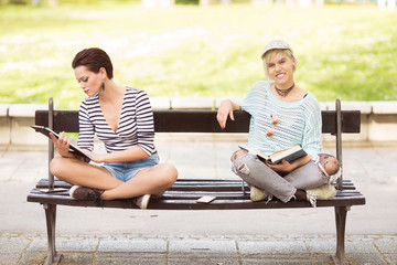 Young students sitting on a bench outdoors and reading
