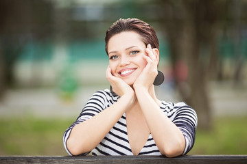 Young woman sitting on a bench outdoors and looking in to a camera