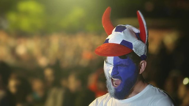 Guy with painted face team flag falls asleep football stadium. Man is yawning at football game against boredom. Against background of crowd, fan closeup bored from lethargic game of football match 4k.
