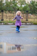 Naklejka premium Little cheerful girl runs through the puddles in rubber boots,