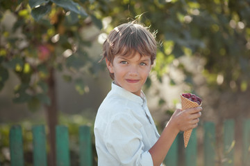Happy handsome boy is eating raspberries in summer garden, outdoor.