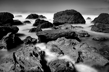 Obraz premium Waves smoothed by long exposure washing in around rocky foreshore.
