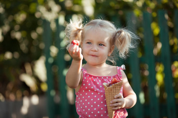 Happy little girl is eating berries in summer garden, outdoor.
