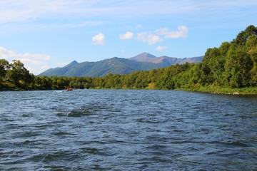 View of Bystraya Malkinskaya river on the Kamchatka Peninsula, Russia. Tourists on orange raft are visible on water.