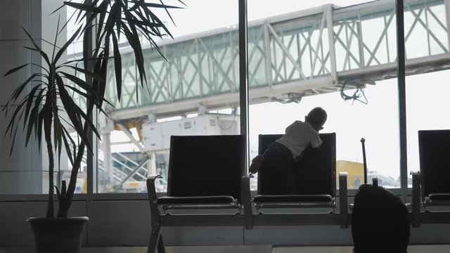 Single baby child silhouette standing on airport chair and look out window