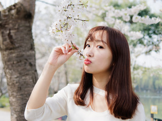 Outdoor portrait of beautiful young Chinese girl smiling among blossom cherry tree brunch in spring garden, beauty, summer, emotion, expression and people lifestyle concept.