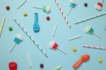 Flat lay childs birthday party, blue background (pattern). Sweet candies, bright balloon, festive candles, cupcake and straws.