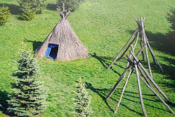 Straw wigwam on a glade on a sunny spring day. Wigwam type thatch huts . © Nataliia