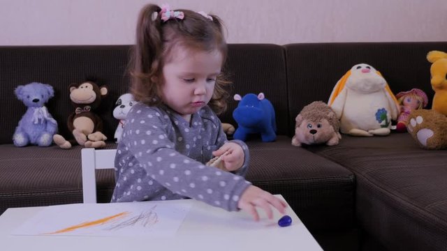 Cute baby girl enthusiastically draws with wax crayons on a piece of paper. 