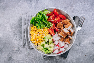 Healthy lunch bowl. Avocado, chicken, tomato, radish, corn, green leaves vegetables salad. Concrete background. Top view. Copy space