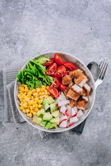 Healthy lunch bowl. Avocado, chicken, tomato, radish, corn, green leaves vegetables salad. Concrete background. Top view. Copy space