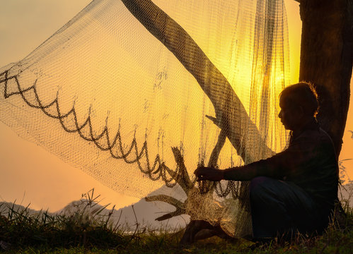 Fisherman repairing fishing net at sunset.