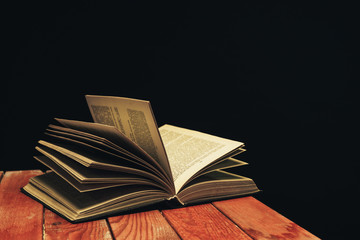 One open old book on a red wooden table. Beautiful dark background.