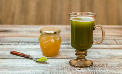 Glass of macha green tea with green tea powder in a spoon and small bottle of honey