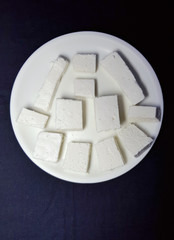 Paneer pieces in white plate on the black background.