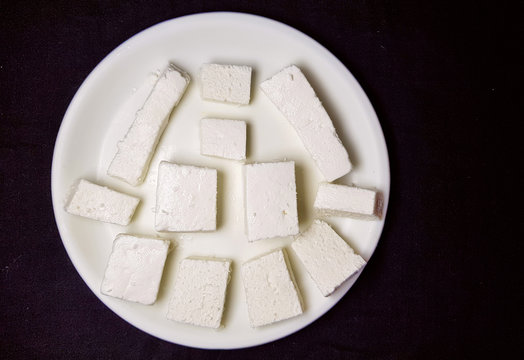 Paneer pieces in white plate on the black background.