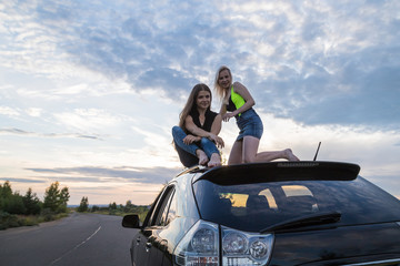 Two girls on the roof of a big black car and white clouds above her