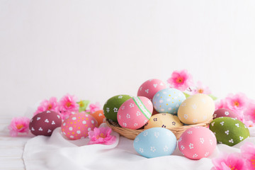 Fototapeta na wymiar Happy easter! Colorful of Easter eggs in nest with flower and Feather on white cheesecloth background.
