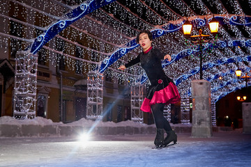 Girl skating on the ice arena in the evening city square in winter