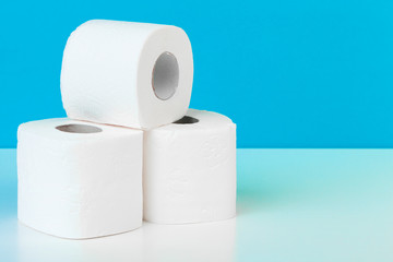 Three toilet paper rolls isolated on white table with blue background