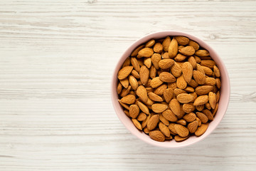 Raw almonds in pink bowl over white wooden surface, top view. Overhead, flat lay, from above. Space for text.