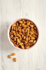 Full pink bowl of almonds over white wooden background, top view. Overhead, flat lay, from above. Close-up.