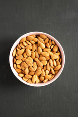Full pink bowl of almonds on black table, overhead view. Flat lay, from above, top view. Closeup.