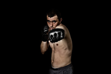 A man in gloves for fighting without rules MMA on a black background. Workout concept, combat training, practicing kick
