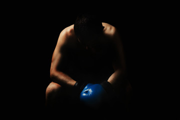 A man in boxing gloves is sitting on a chair in the corner of the ring against a dark background....